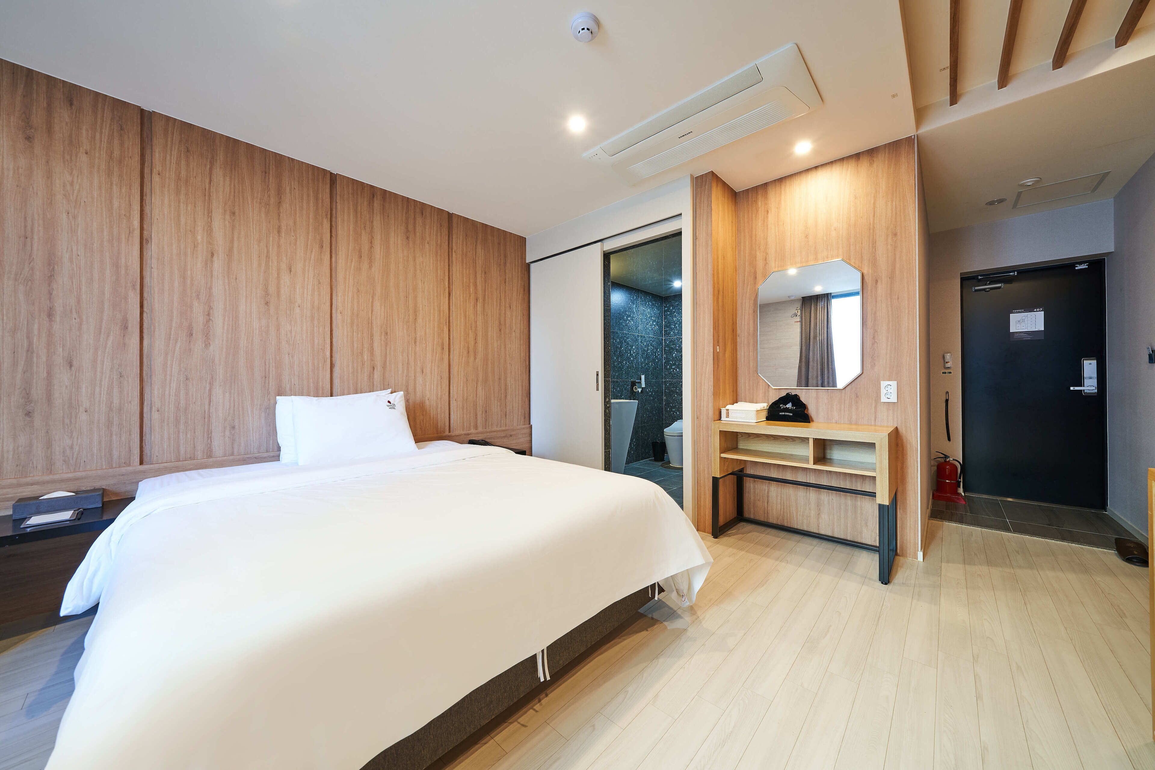 A modern hotel room with a large bed, wooden paneling, a built-in desk, and a mirror.