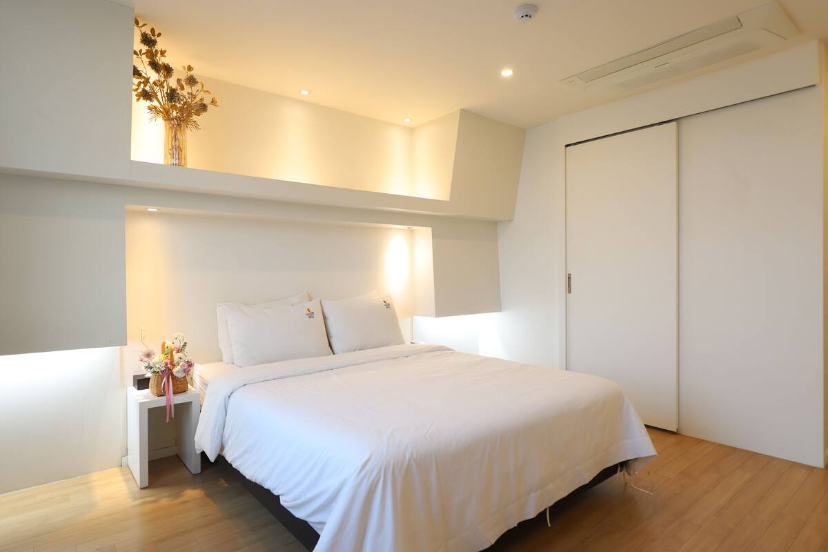A modern bedroom with a large bed, a nightstand with a vase of flowers, and a wardrobe.