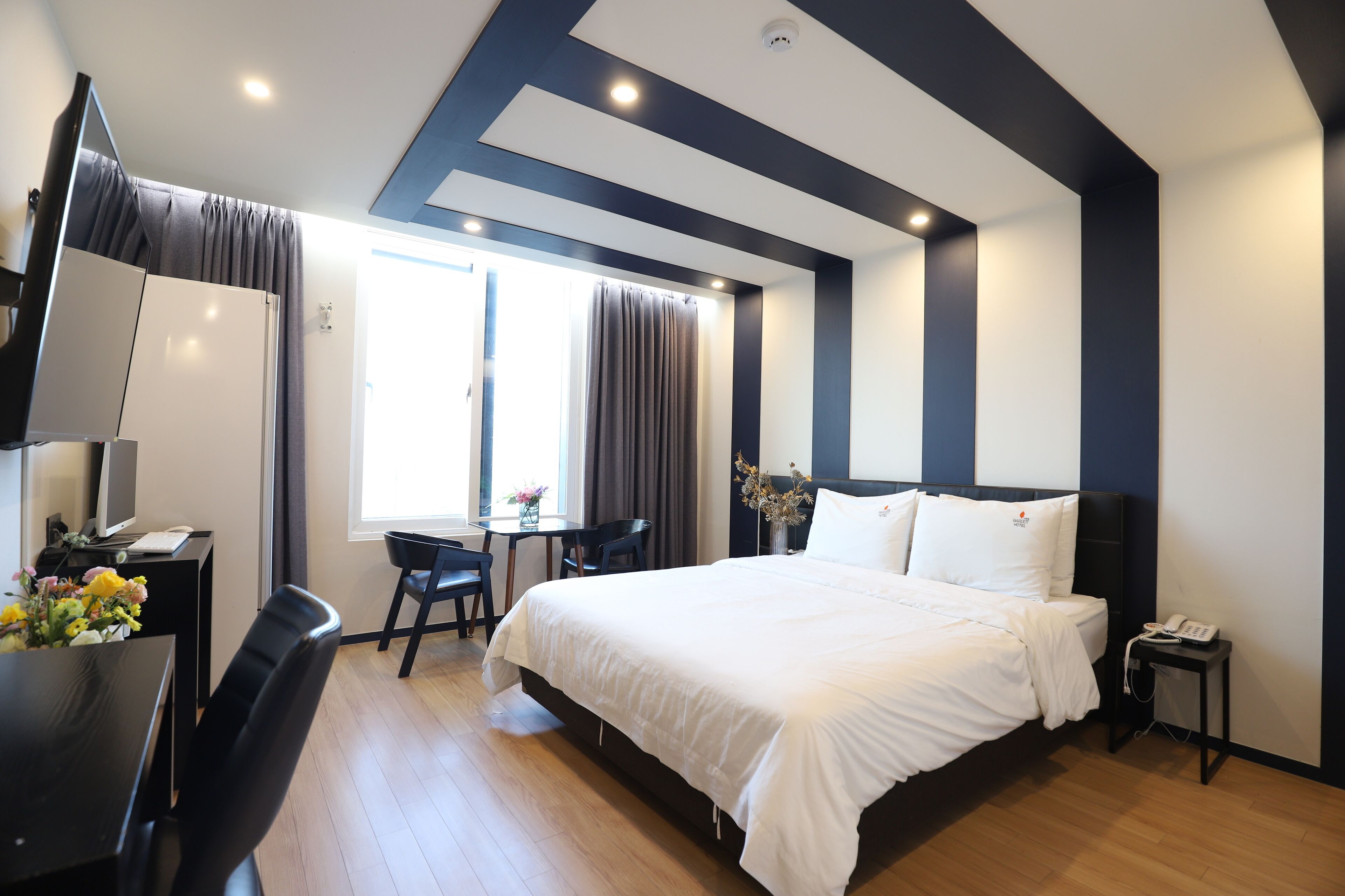 A modern hotel room with a large bed, a desk with a chair, a small table, and a TV.