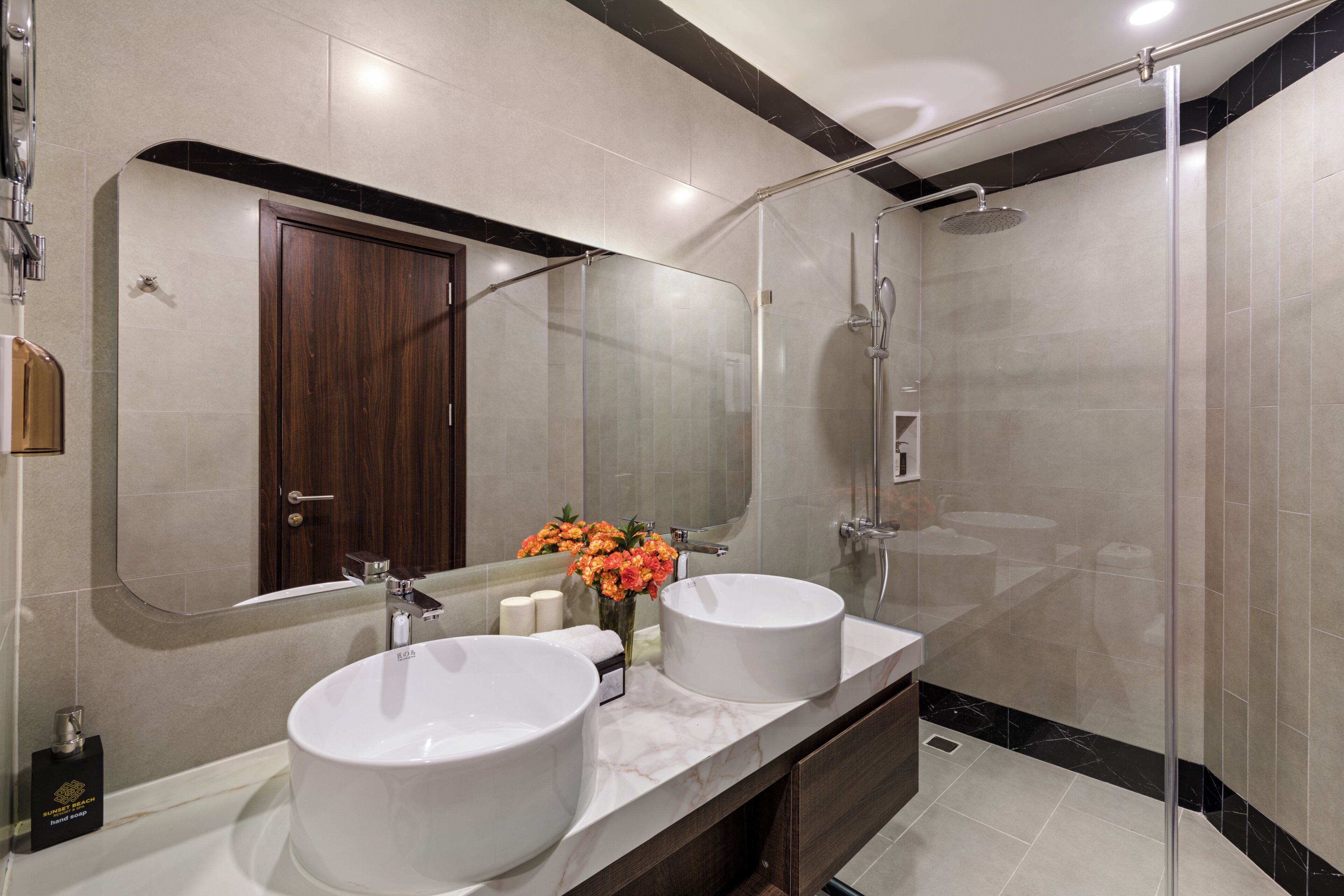 Une salle de bain moderne avec deux lavabos, une douche à l’italienne en verre et un grand miroir.
