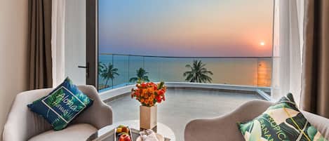 Un balcon avec vue sur le coucher de soleil, une table garnie de fruits et de fleurs, et deux canapés agrémentés de coussins aux motifs tropicaux.