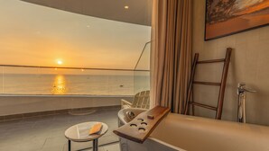 A balcony with a view of the sunset over the ocean, a bathtub, a towel, and a small table with a book. - Sunset Beach Resort & Spa- Beachfront Pirate Fire Show (Phu Quoc)
