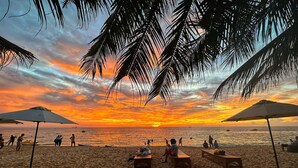 A beach with sun loungers and umbrellas, a clear view of the sunset over the ocean, and people enjoying the beach. - Sunset Beach Resort & Spa- Beachfront Pirate Fire Show (Phu Quoc)