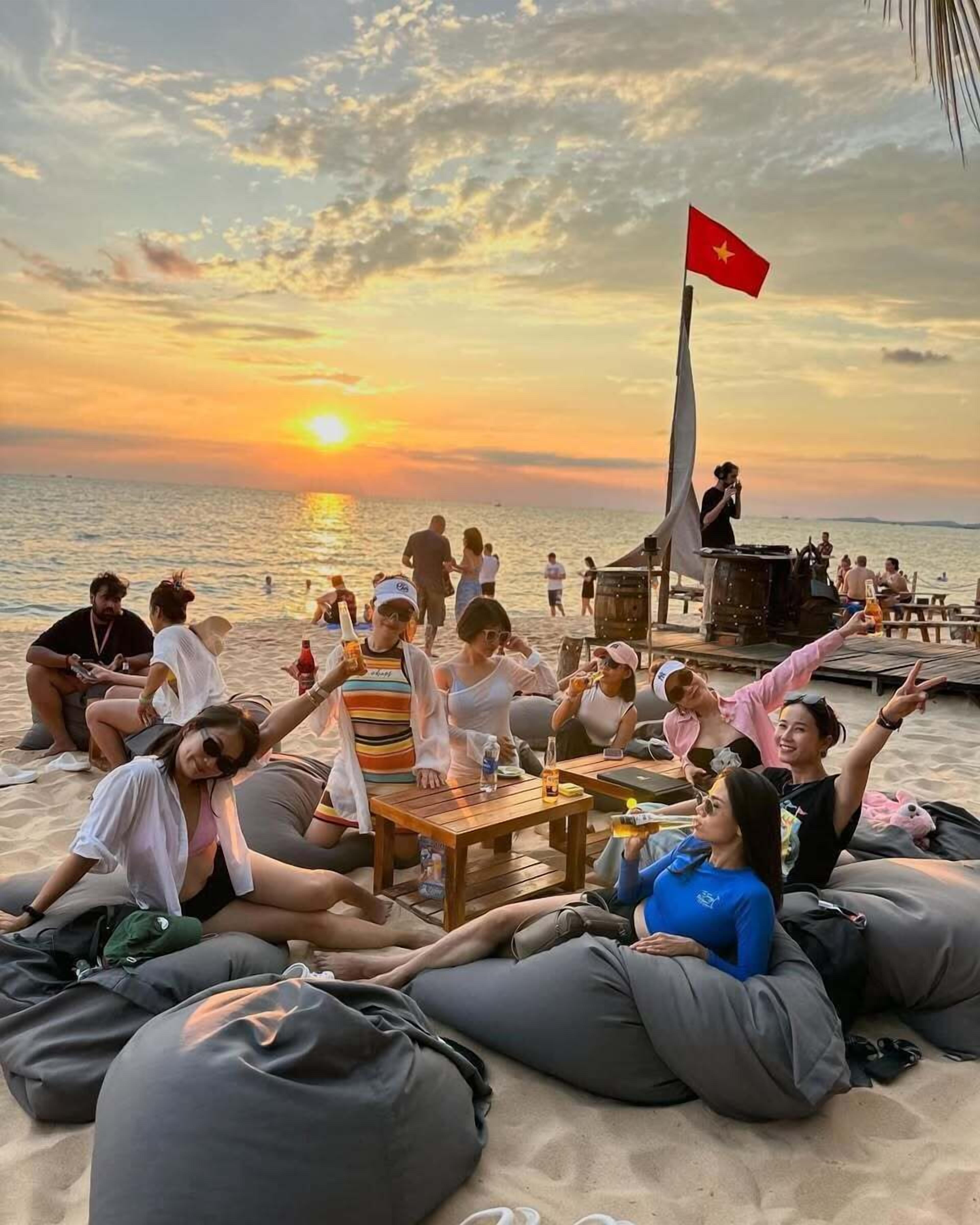 Un groupe de personnes se détend sur des fauteuils en forme de sac de haricots sur une plage, au coucher du soleil.