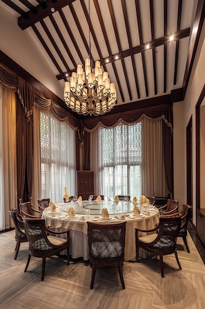 A dining area with a round table set for six, surrounded by wicker chairs, under a large chandelier. - Wuzhishan Yatai Rainforest Hotel (Wuzhishan)