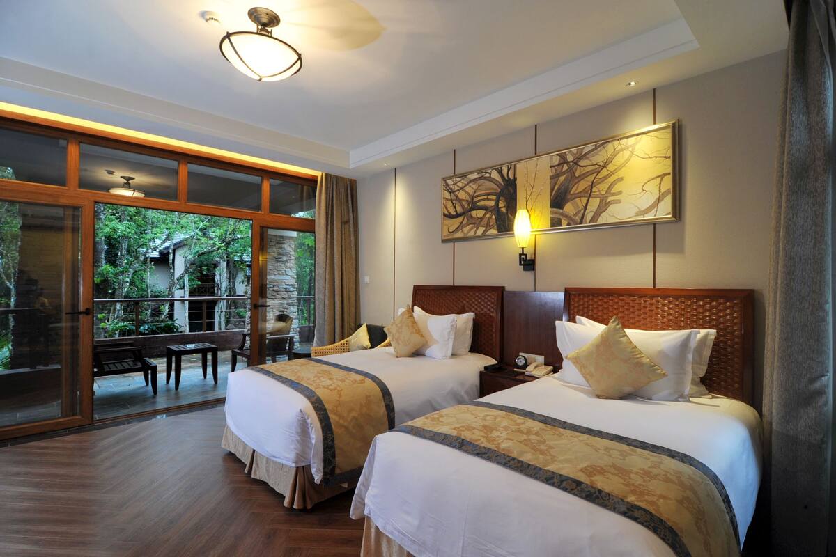 Habitación de hotel con dos camas, un ventanal grande y vista a zonas verdes.