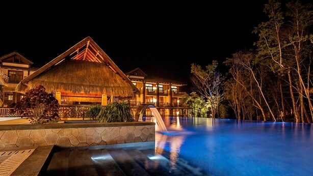 A resort with a pool, thatched-roof buildings, and a stone wall.
