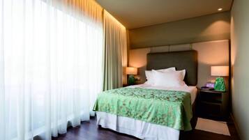 Ein Hotelzimmer mit einem großen Bett, einem Nachttisch mit Lampe und transparenten Vorhängen am Fenster.