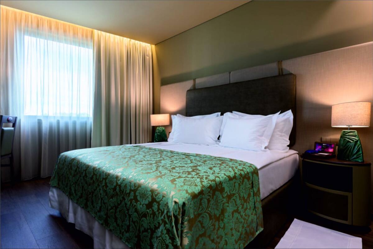 Ein Hotelzimmer mit Bett, Schreibtisch, Stuhl und Nachttisch mit Lampe.