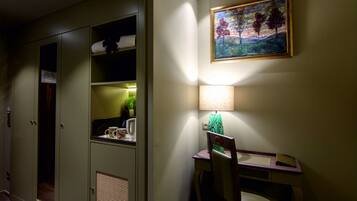 A hotel room with a desk, chair, lamp, and a painting on the wall.