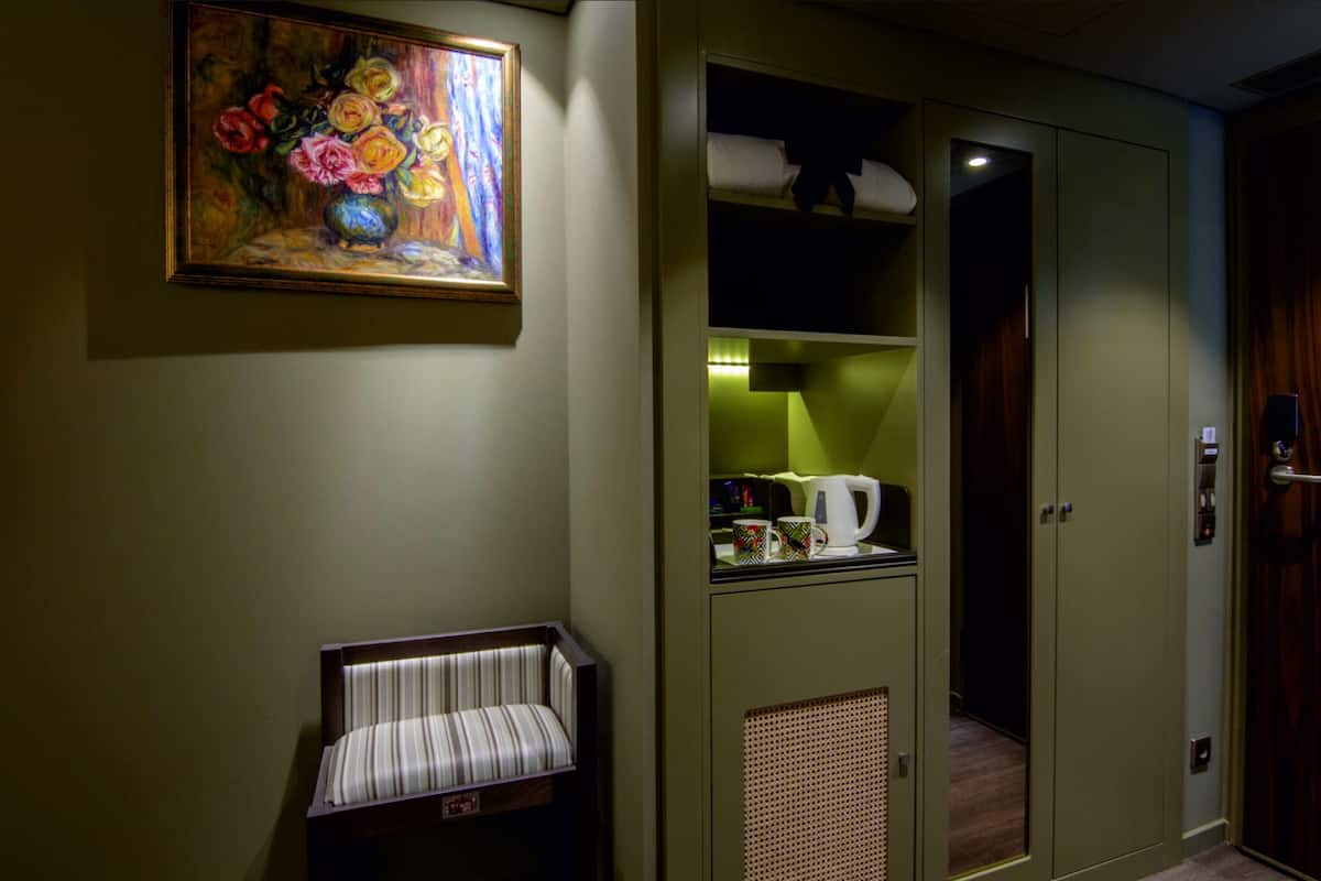 Ein Zimmer mit einer gestreiften Bank, einem Blumenbild und einer Küchenzeile mit Wasserkocher sowie einem Kleiderschrank.