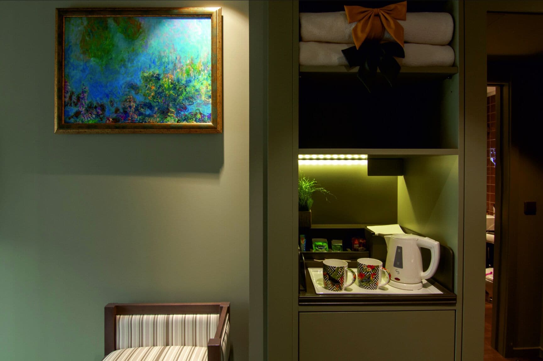 Een hotelkamer met een bed, een schilderij, een plank met handdoeken en een koffiezetapparaat.