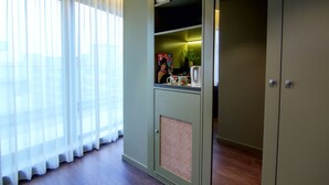Una habitación con un ventanal grande, una kitchenette con cafetera y un mueble con estantes.