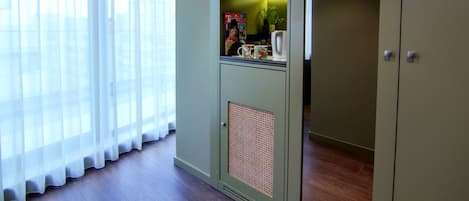 A room with a large window, a kitchenette with a coffee maker, and a cabinet with shelves.