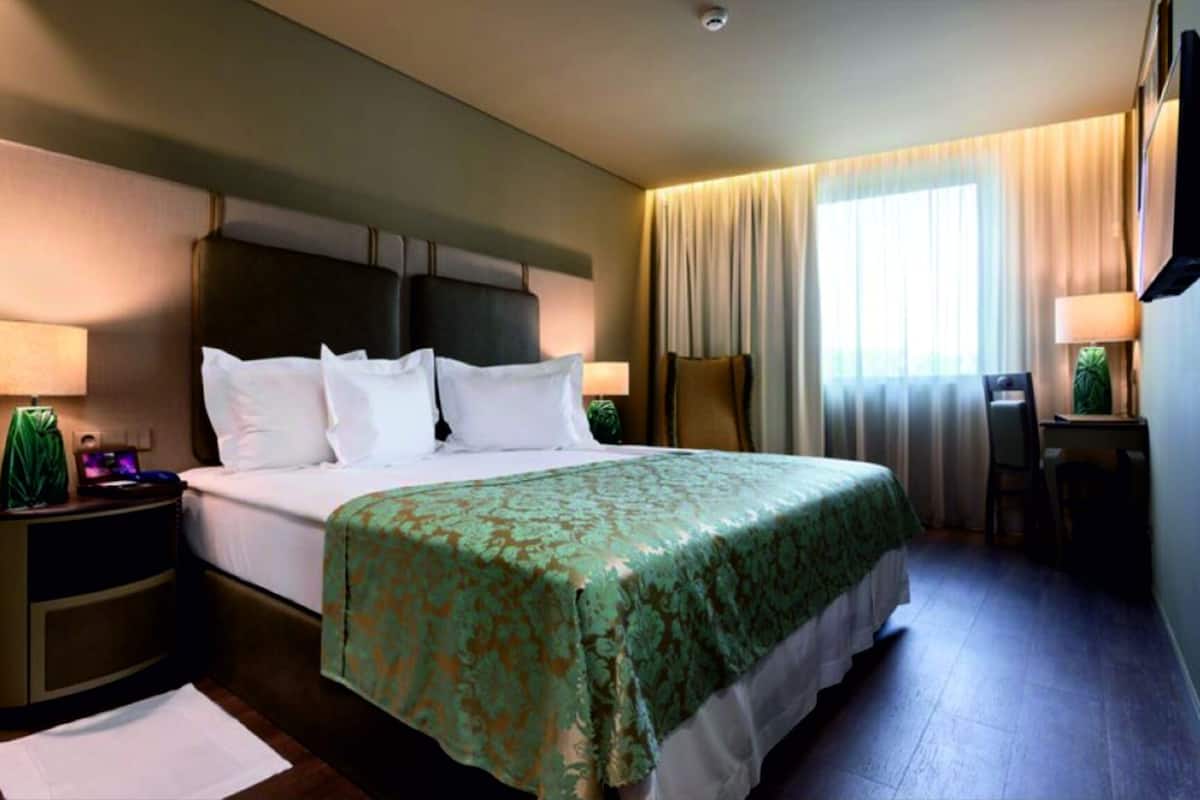 Ein Hotelzimmer mit einem großen Bett, einem Schreibtisch, einem Stuhl und einem Fenster mit Vorhängen.