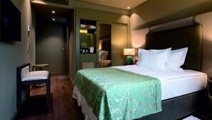 Habitación de hotel con cama, una silla, una mesita, un espejo y televisor en la pared.