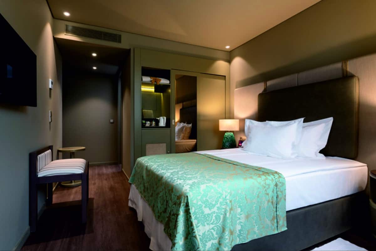 Ein Hotelzimmer mit Bett, Sessel, kleinem Tisch, Spiegel und Fernseher an der Wand.