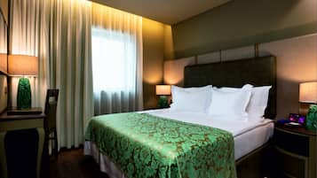 Habitación de hotel con una cama grande, dos mesitas de noche, un escritorio con silla y una ventana con cortinas.