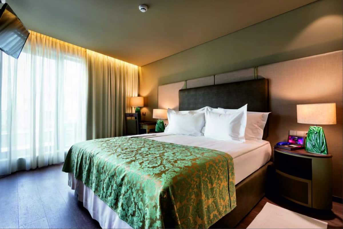 Ein Hotelzimmer mit einem großen Bett, zwei Nachttischen, einer Kopfteil und einem Fenster mit Vorhängen.