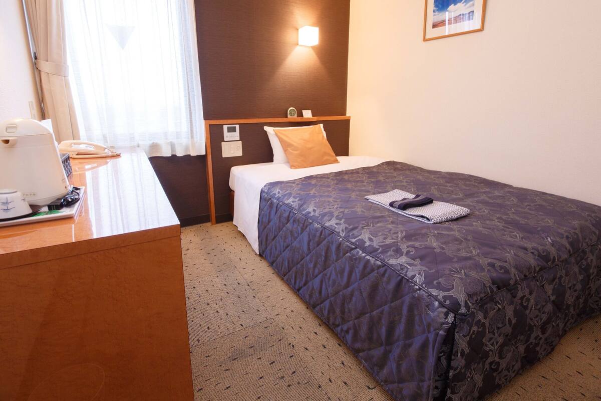 Een hotelkamer met een bed, nachtkastje, lamp en een ingelijst schilderij aan de muur.