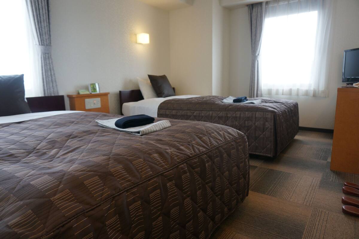 Een hotelkamer met twee bedden, een televisie, een nachtkastje en een raam met gordijnen.