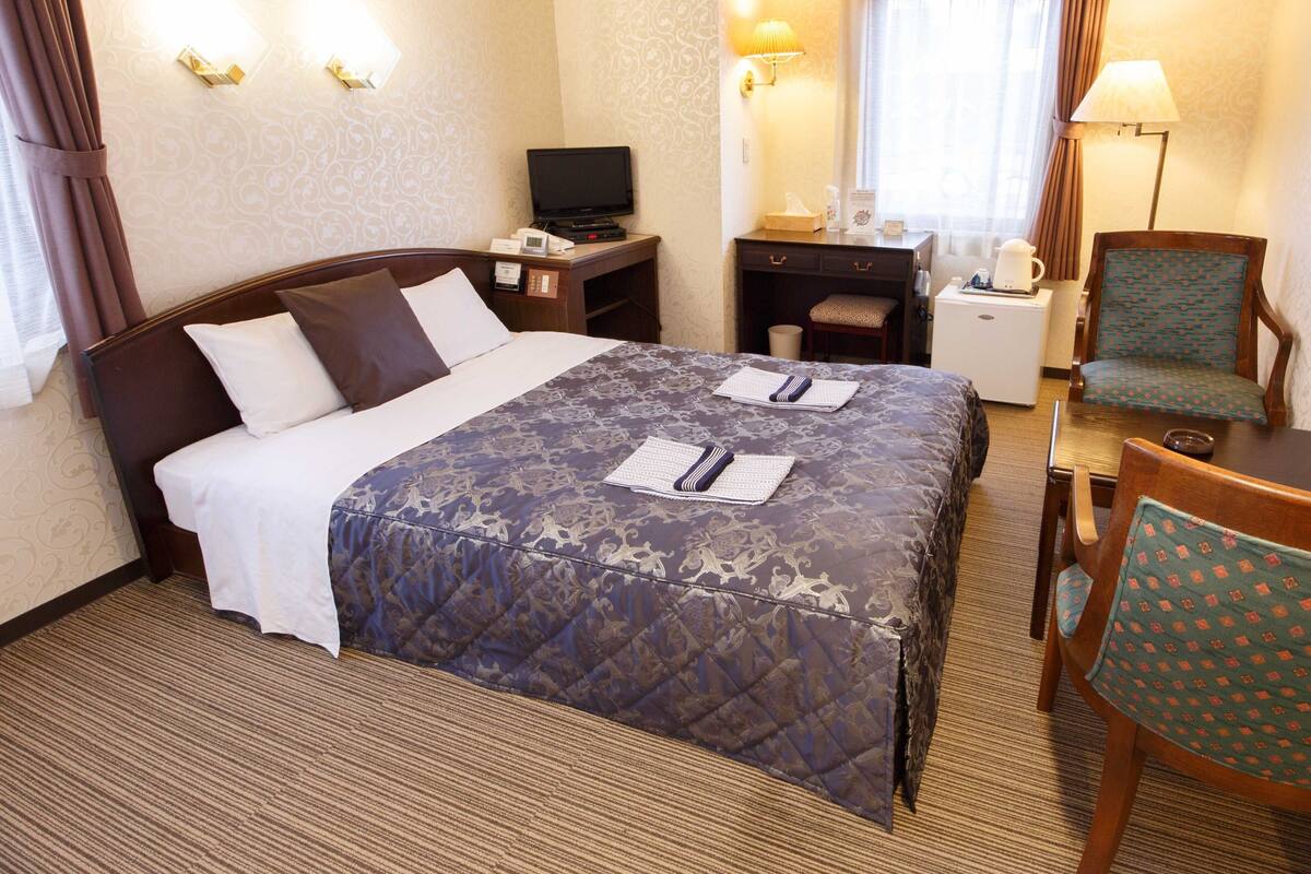Een hotelkamer met een bed, een bureau, een stoel, een televisie en een lamp.