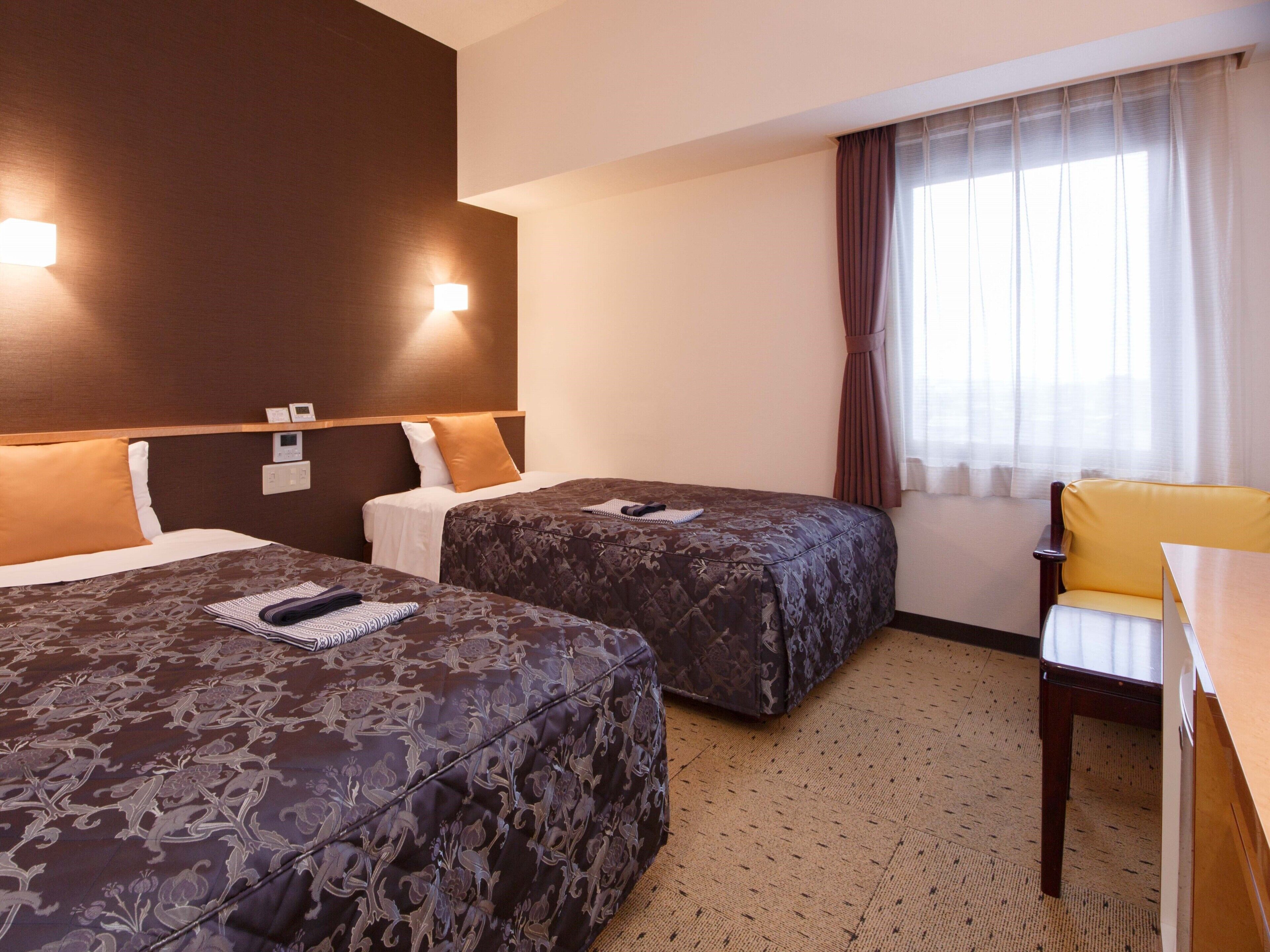 Une chambre d’hôtel avec deux lits, un bureau, une chaise et une fenêtre avec des rideaux.