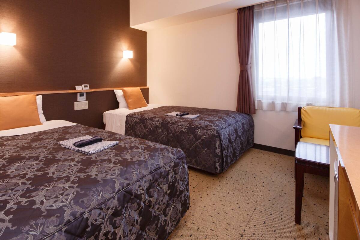 Een hotelkamer met twee bedden, een bureau, een stoel en een raam met gordijnen.