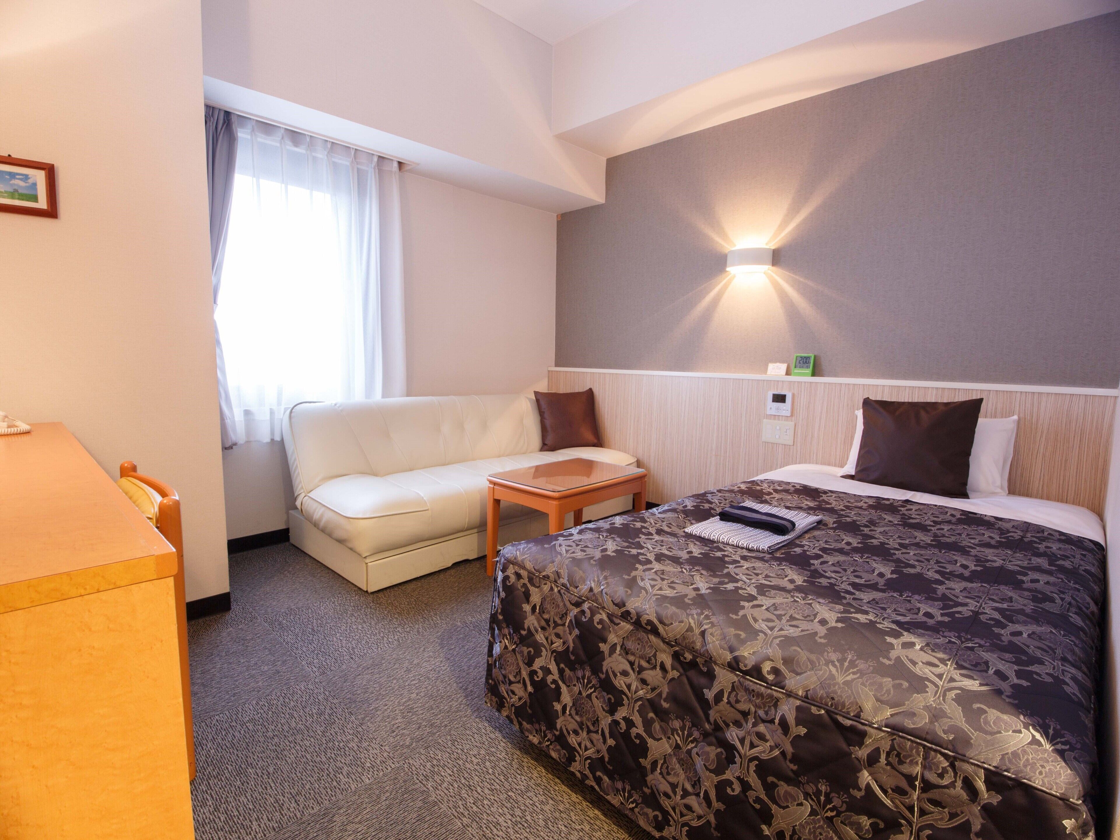 Une chambre d’hôtel avec un lit, un canapé, une petite table, un bureau et une fenêtre avec des rideaux.