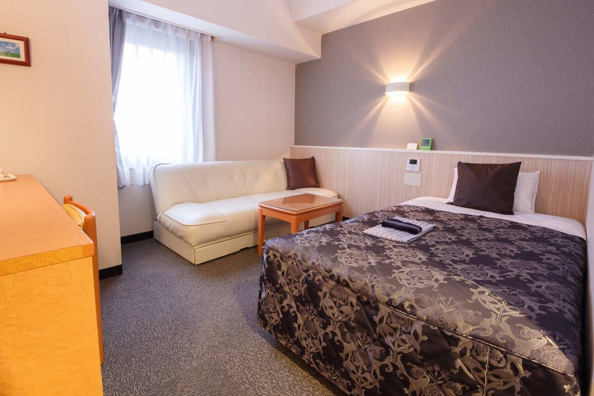Een hotelkamer met een bed, een bank, een tafeltje, een bureau en een raam met gordijnen.