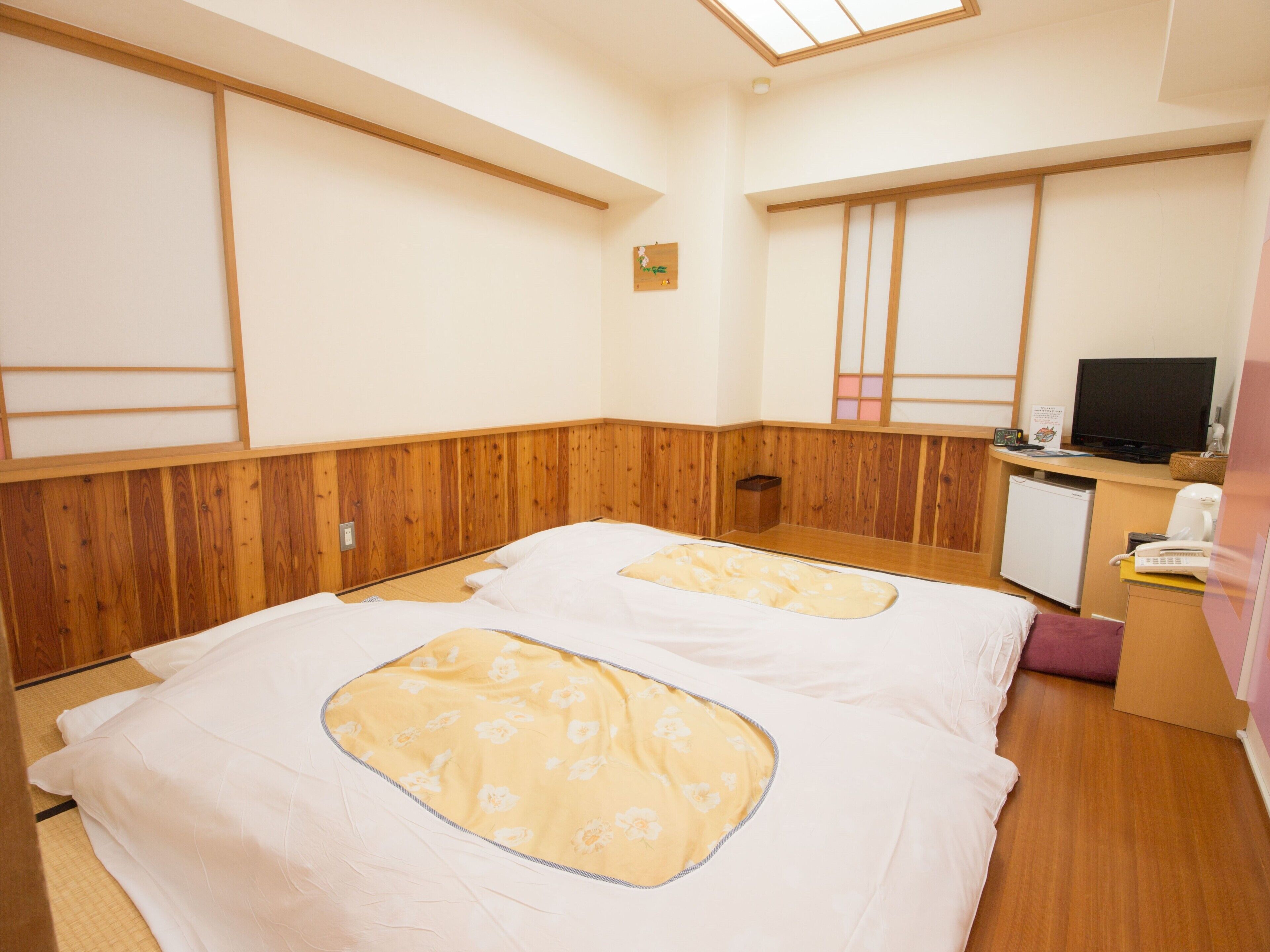 Une chambre avec deux lits, un bureau avec un ordinateur et un petit réfrigérateur.