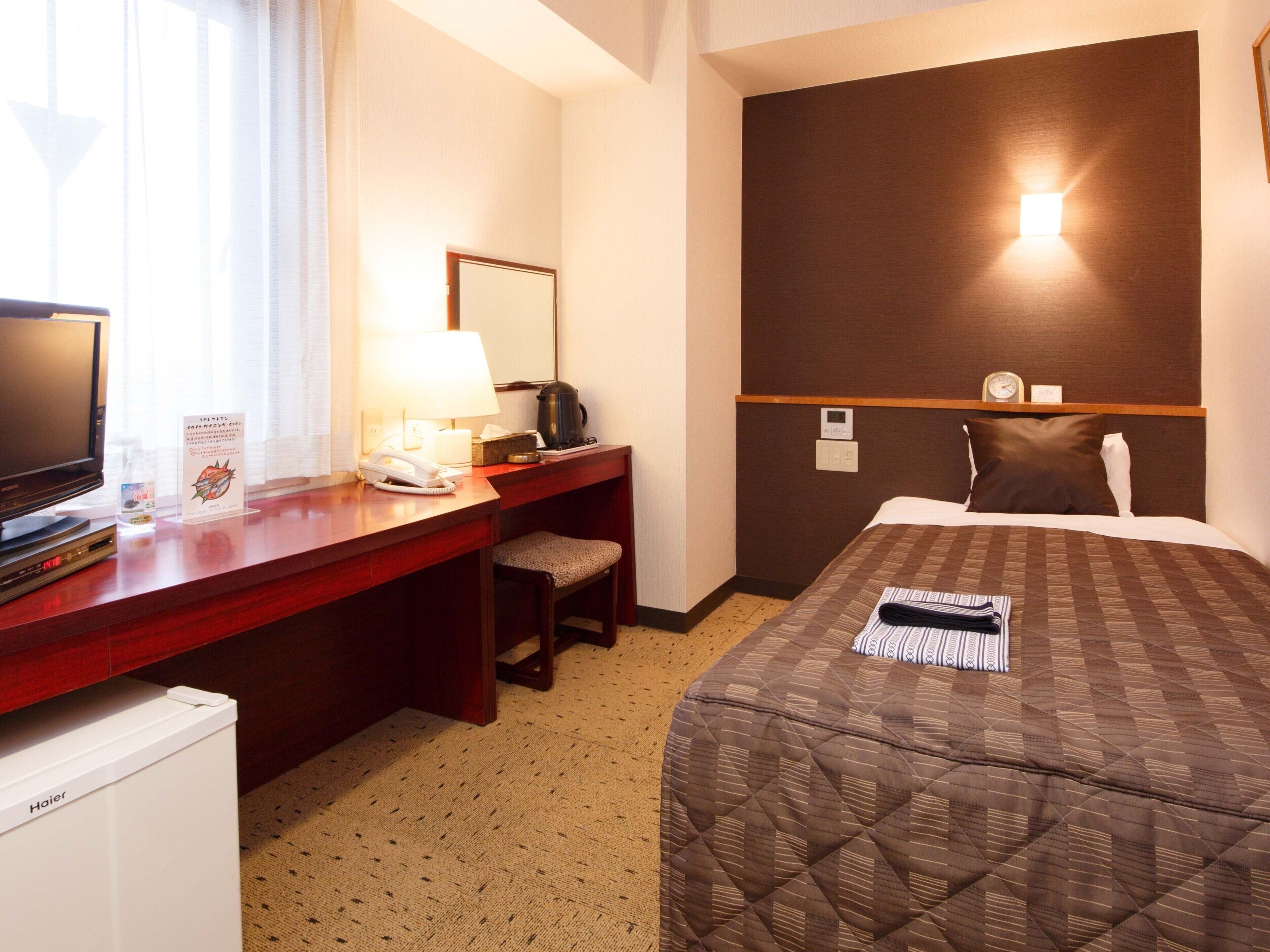 Une chambre d’hôtel équipée d’un lit, d’un bureau avec un téléphone, d’une machine à café, d’une télévision et d’une horloge murale.