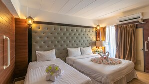 A hotel room with two beds, a tufted headboard, wall-mounted lamps, an air conditioning unit, and a window with curtains. - Sudyod House (Bangkok)