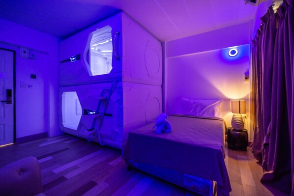 A room with a bunk bed, a small table with a lamp, and a window with curtains.