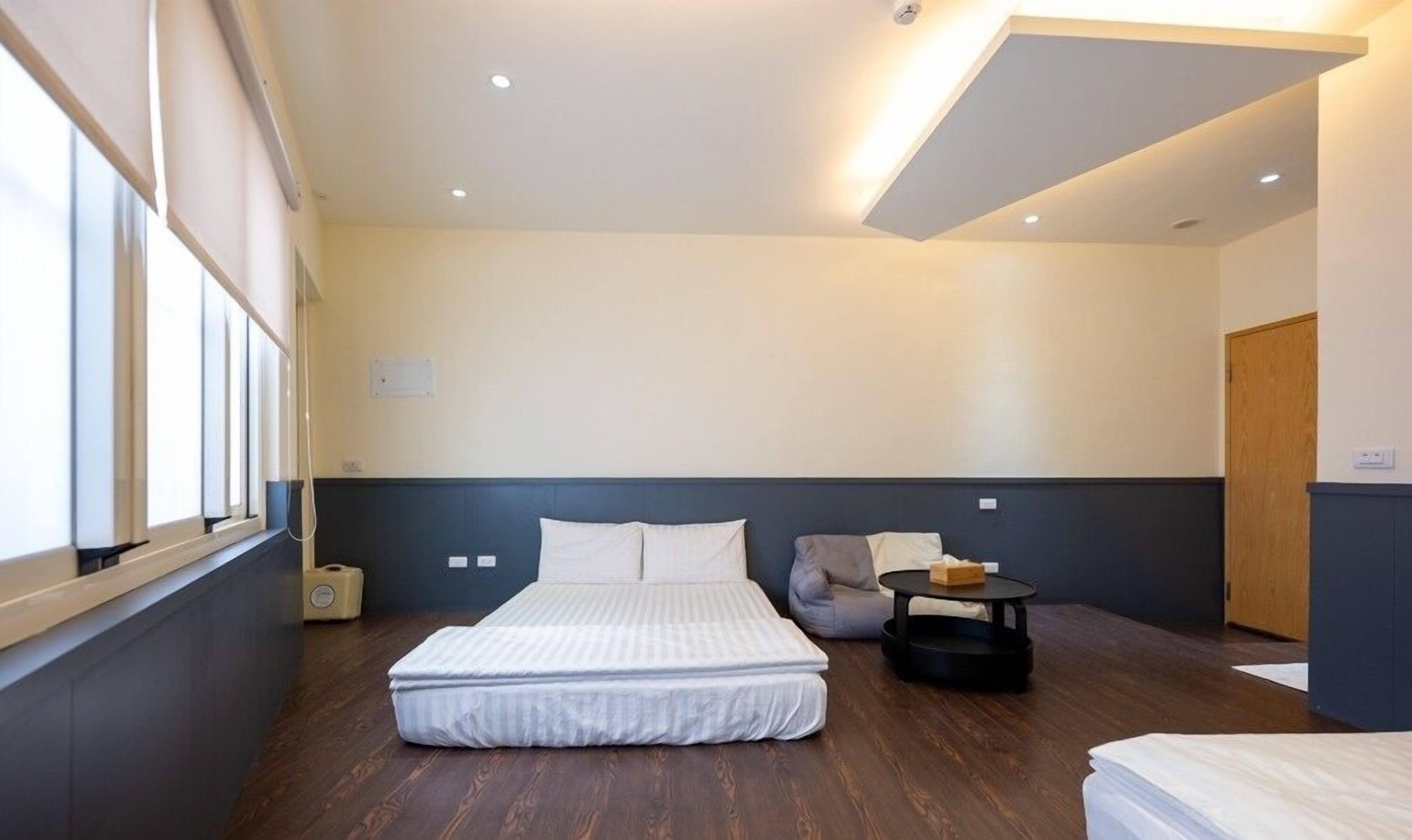 A modern hotel room with a large bed, a small round table, and a window with blinds.