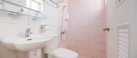 Un baño con lavamanos, inodoro y ducha blancos. Hay una repisa de vidrio sobre el lavamanos y un perchero en la pared.