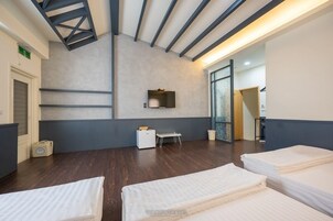 Habitación de hotel con techo alto, suelo de madera, una cama, una mesita y un estante fijado a la pared.