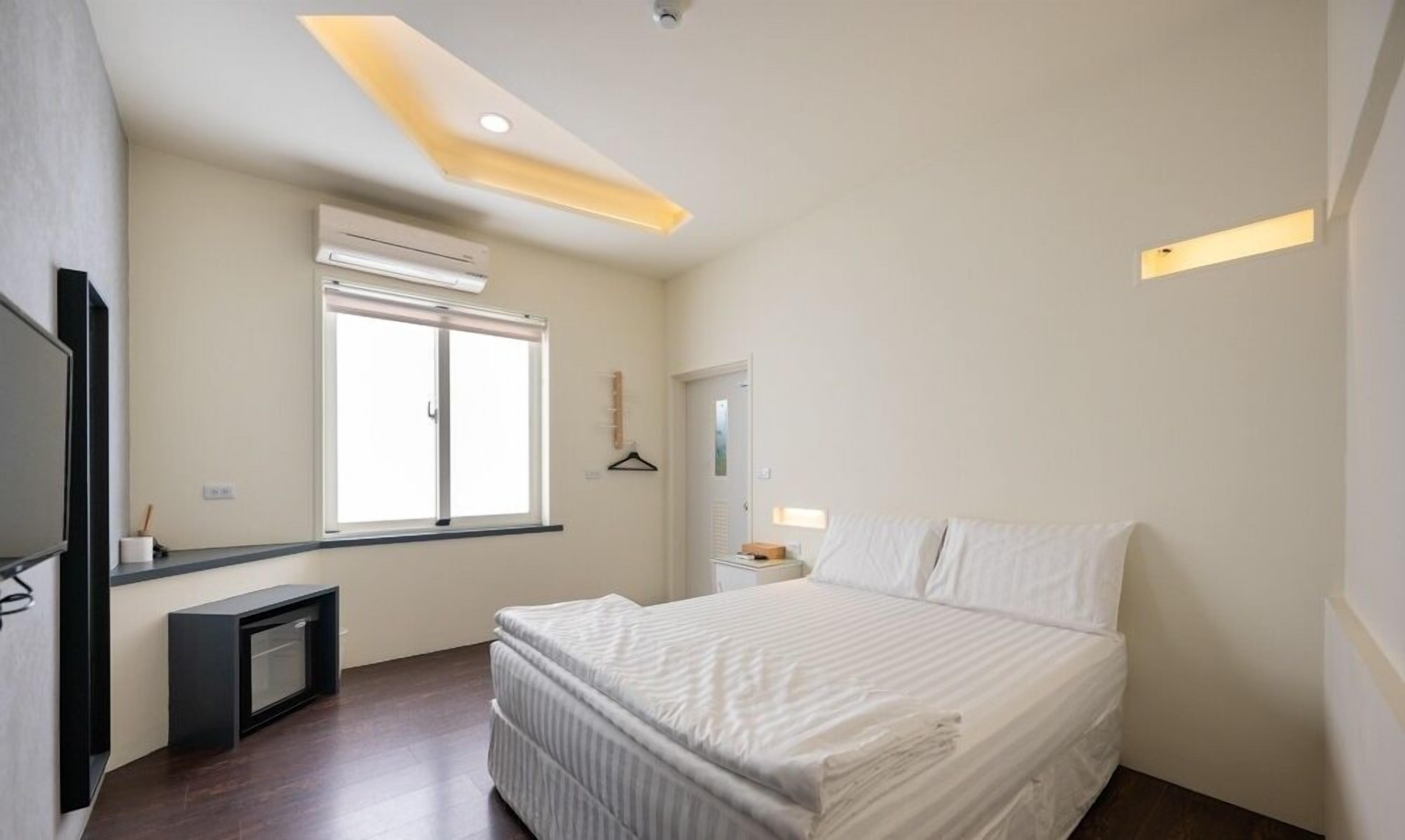 Un dormitorio moderno con cama, ventana, aire acondicionado y un pequeño escritorio.