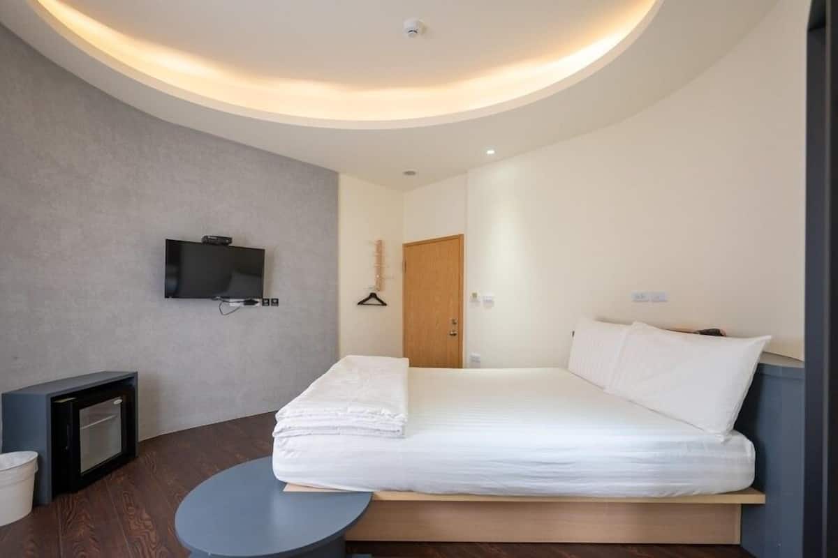 Una habitación de hotel moderna con una cama grande, un televisor de pantalla plana en la pared, una mesita y una puerta de madera.