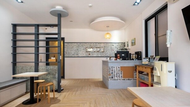 Una cafetería moderna con suelo de madera, una barra con una máquina de café y un área de estar con mesas y sillas.