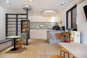 Una cafetería moderna con suelo de madera, una barra con una máquina de café y un área de estar con mesas y sillas.