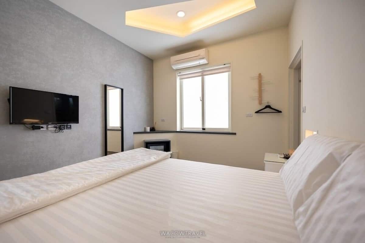 Una habitación de hotel moderna con una cama, un televisor de pantalla plana montado en la pared, una ventana con persianas y una mesita de noche.
