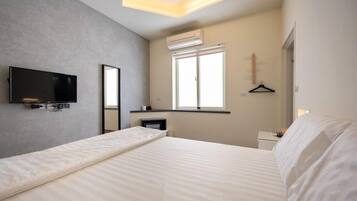 Quarto de hotel moderno com cama, televisão de tela plana na parede, janela com persianas e mesa de cabeceira pequena.