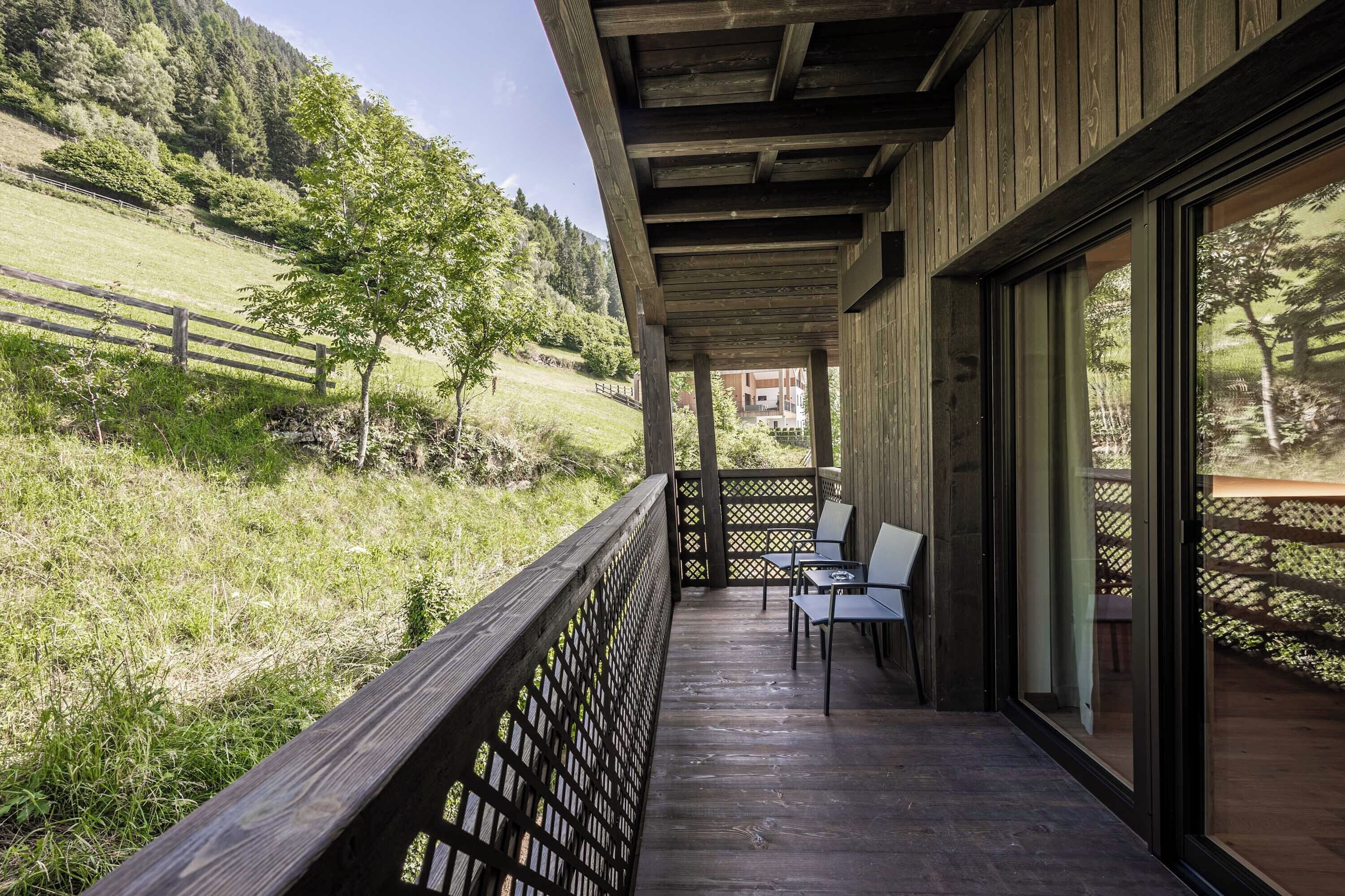 A wooden deck with outdoor seating, overlooking a grassy hillside and a building in the background.