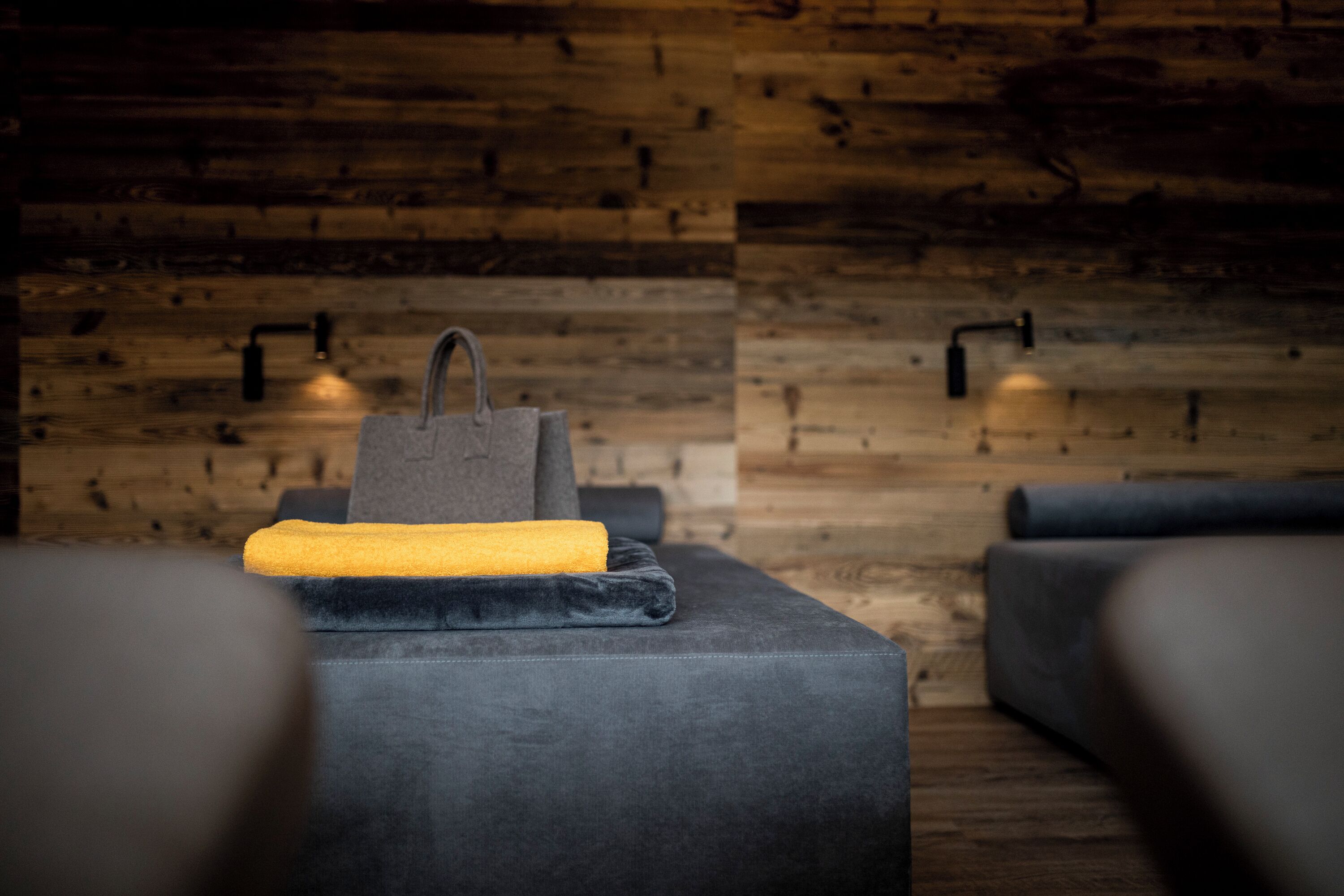 Una habitación con pared de madera, un sofá gris, una toalla amarilla y un bolso gris.
