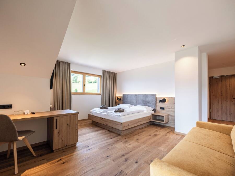 A modern bedroom with a wooden desk, a bed with a headboard, a sofa, and a window with curtains.