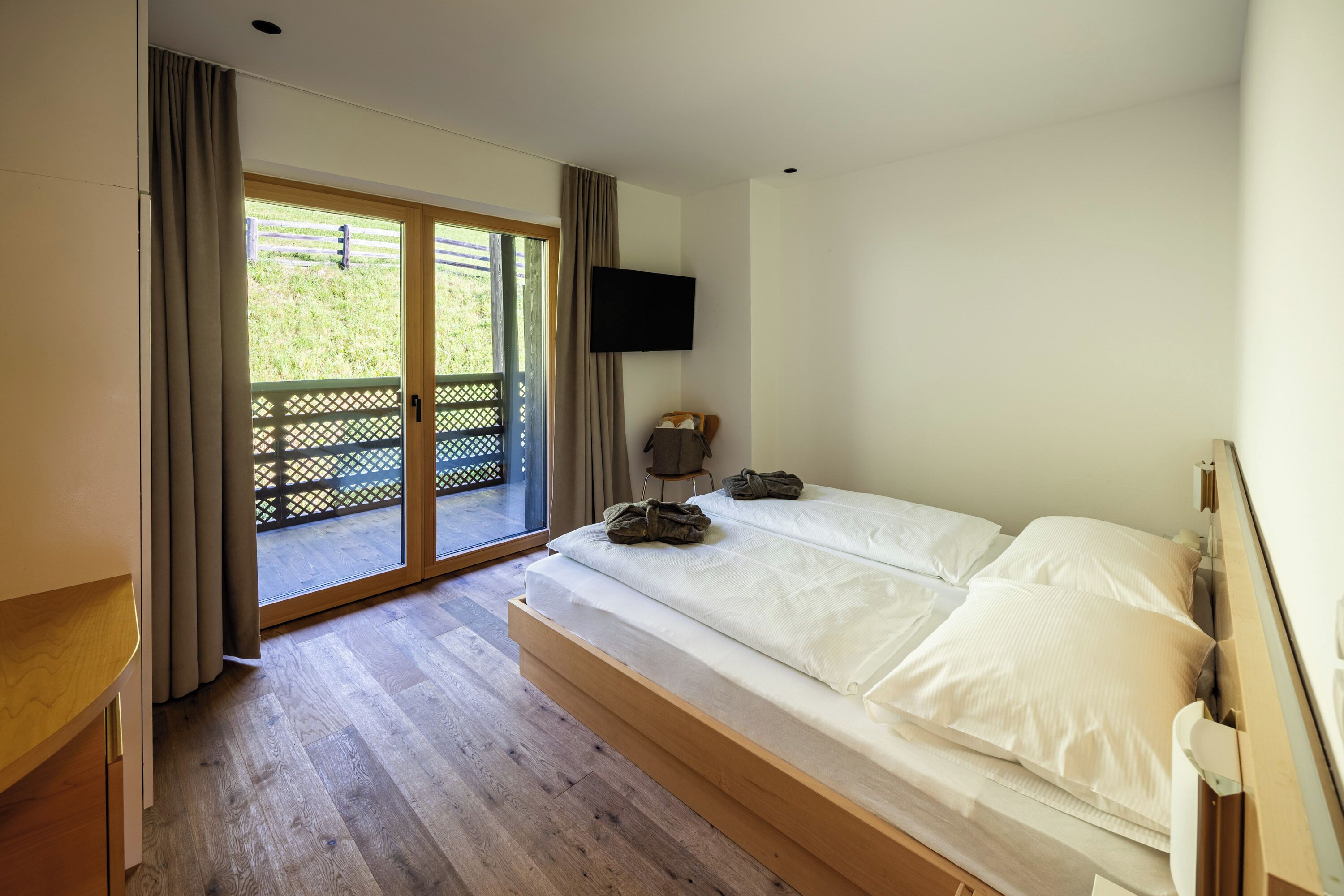 A bedroom with a large bed, a TV mounted on the wall, and a sliding glass door leading to an outdoor area.