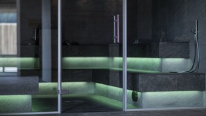 A modern bathroom with a glass partition, a green-lit bench, and a shower area. - Hotel Rommisa (Perca)