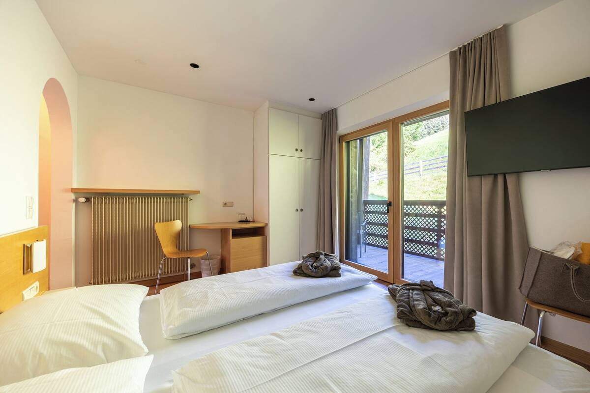 A hotel room with a bed, a desk, a chair, a TV, and a window with curtains.