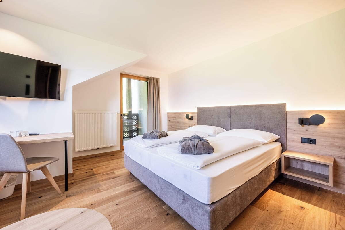 A modern hotel room with a large bed, a desk, and a TV mounted on the wall.